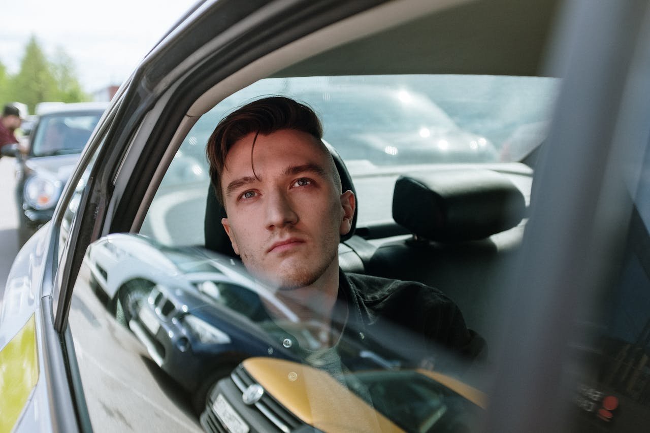 Young man gazes thoughtfully through a taxi window amidst urban traffic, enjoying the ride.