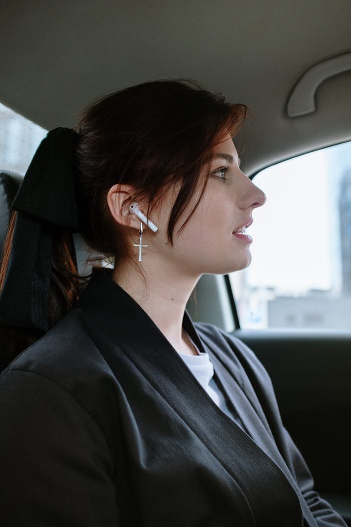 Side profile of a woman wearing AirPods and earrings in a car, focused and attentive.