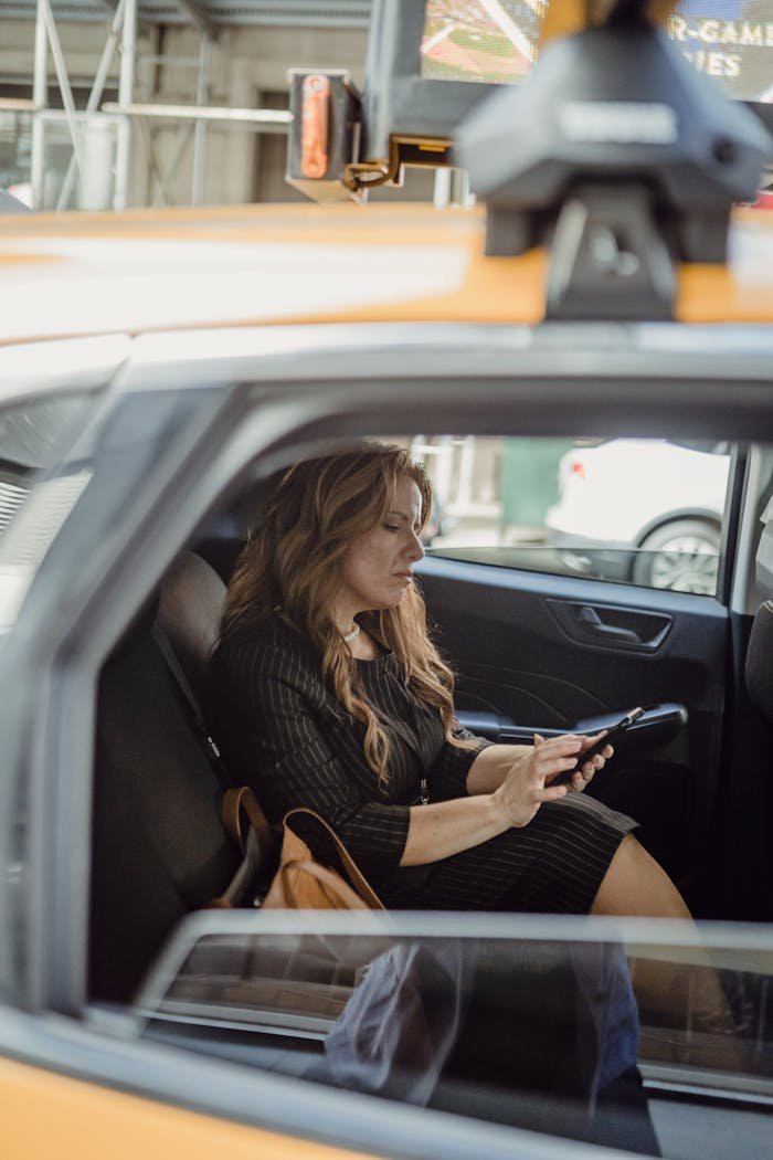 Woman sitting in taxi, focused on smartphone, urban background visible.